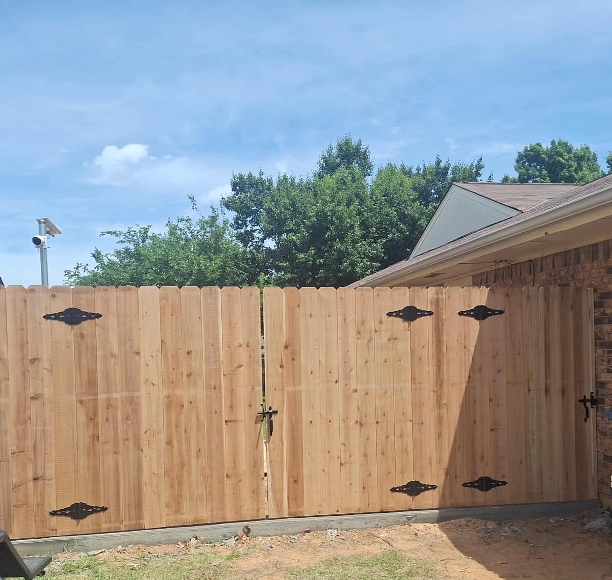 Cedar wood double drive gate with decorative black strap hinges, built by SWY Fencing under a blue Oklahoma sky