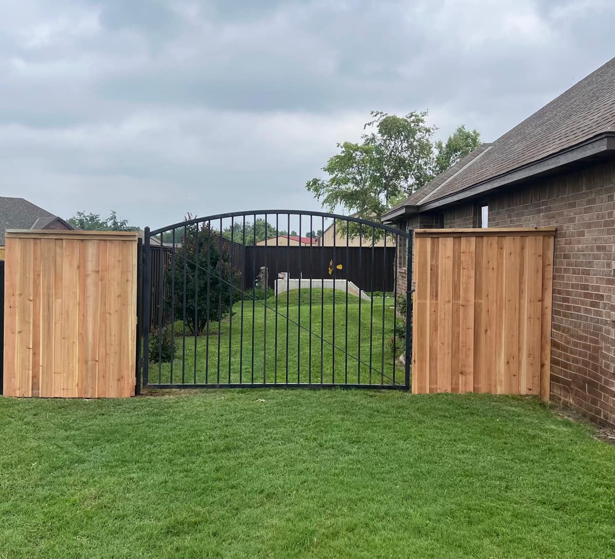 Arched black ornamental iron entry gate flanked by cedar privacy panels beside an Oklahoma City home